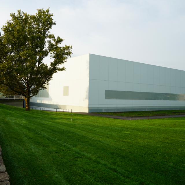 A white rectangular building is surrounded by a green lawn and green trees. 