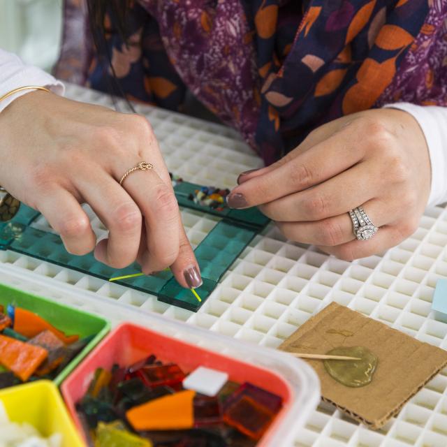 An adult adds pieces of multicolored cut glass to a transparent green frame
