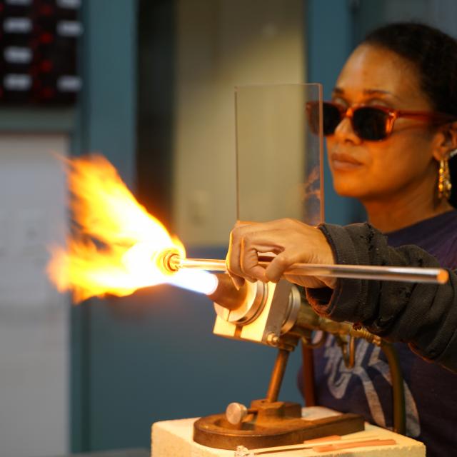 A woman heats glass at a flameworking torch in the Studio