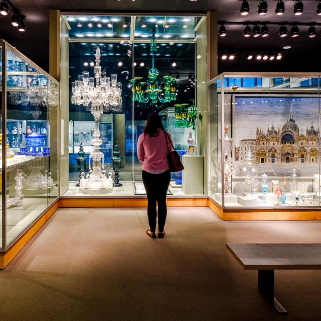 A guest stands in the middle of a gallery of glass objects in exhibit cases